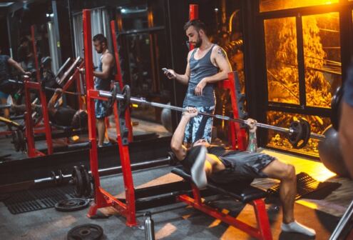 Benefits of lifting weights, a man on his phone and a man who is doing bench press